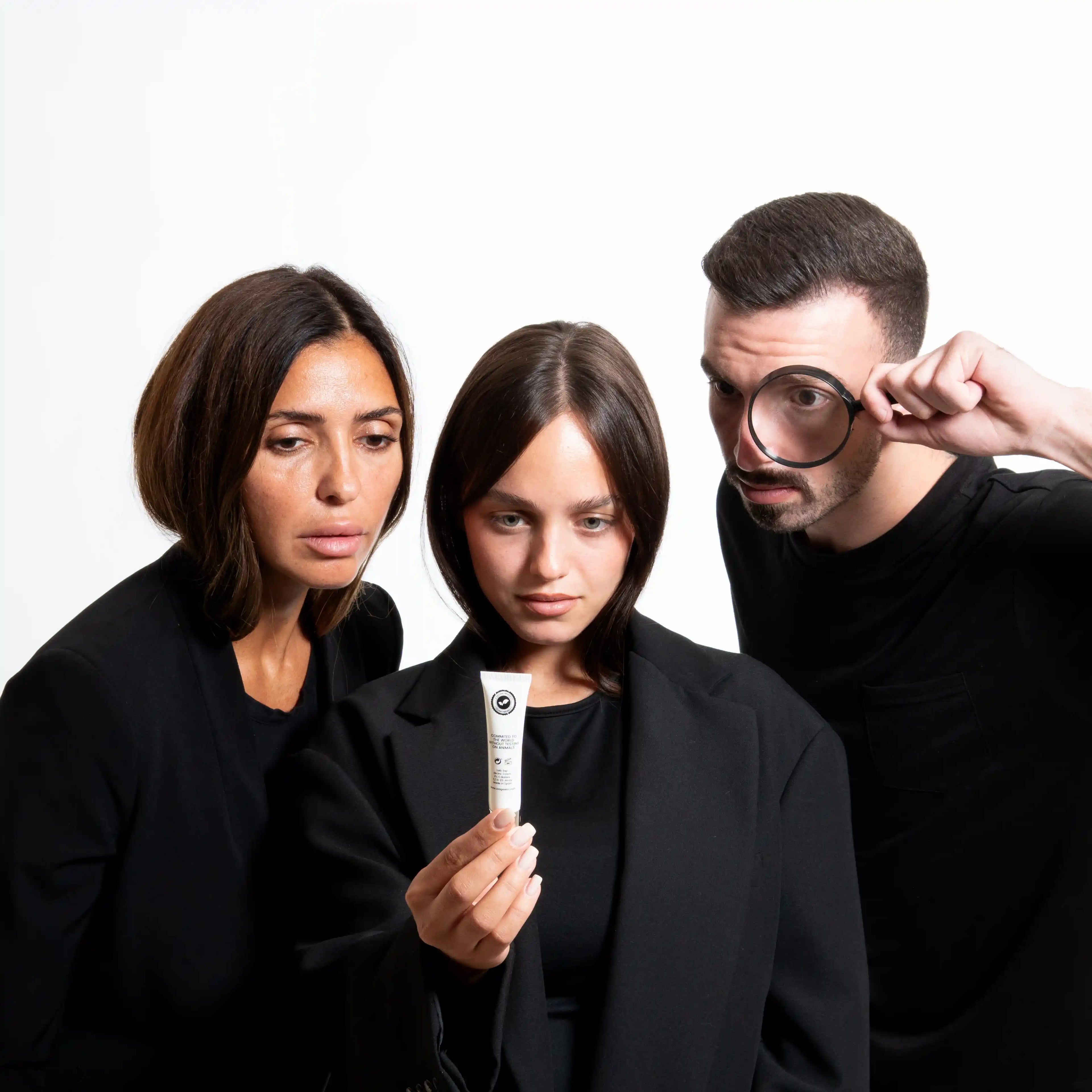 Three people in black outfits with a product and a magnifying glass on a white background